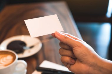 Elinde beyaz, boş bir kartvizit, üzerinde defter ve kahve fincanı olan bir el. 