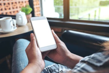 Modern kafede kahve fincanı olan beyaz bir cep telefonu kullanan ve el ele tutuşan bir kadının görüntüsü.