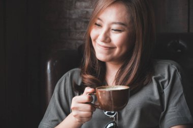 Güzel bir Asyalı kadının sıcak kahveyi kucağında tutarken ve içerken görüntüsü.