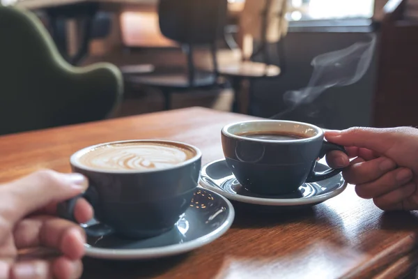 カフェの木のテーブルの上にコーヒーとホットチョコレートカップを持っている2人の手のイメージを閉じます — ストック写真