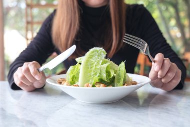 Restoranda bıçak ve çatalla sezar salatası yiyen bir kadının yakın plan görüntüsü.