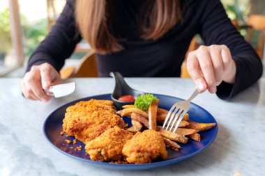 Restoranda kızarmış tavuk ve patates kızartması yemek için çatal ve bıçak kullanan bir kadının yakın plan görüntüsü.