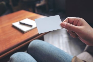 Tahta üzerinde defter olan beyaz, boş bir kartvizit tutan bir el. 