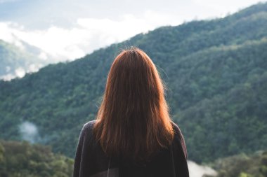 Sisli bir günde tek başına duran ve dağlara bakan bir kadın. Mavi gökyüzü arka planında sabah.