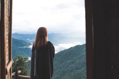 Sisli bir günde tek başına duran ve dağlara bakan bir kadın. Mavi gökyüzü arka planında sabah.