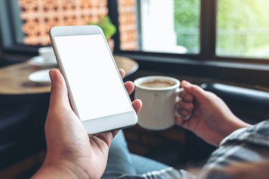 Modern kafede kahve içerken beyaz cep telefonunu boş ekran ile tutan ellerin görüntüsü.