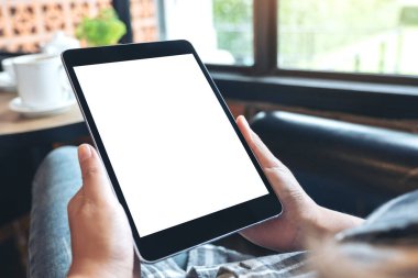 Kafede otururken boş beyaz masaüstü ekranlı siyah tableti tutan ellerin görüntüsü