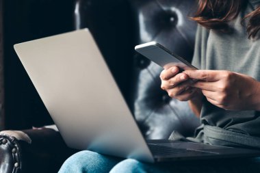 Dizüstü bilgisayarla çalışırken cep telefonu kullanan bir kadın. 