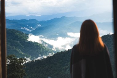 Sisli bir günde tek başına duran ve dağlara bakan bir kadın. Mavi gökyüzü arka planında sabah.