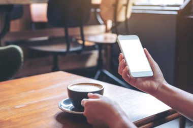 Modern kafede kahve içerken beyaz cep telefonunu boş ekran ile tutan ellerin görüntüsü.