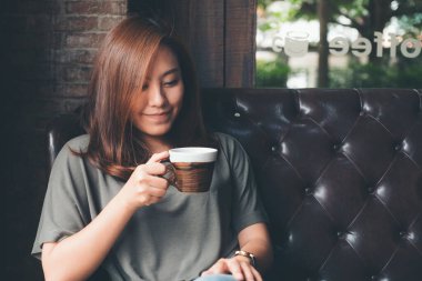 Güzel bir Asyalı kadının sıcak kahveyi kucağında tutarken ve içerken görüntüsü.