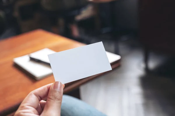 一只手拿着白色的空白名片 上面有笔记本在木制桌子上 — 图库照片