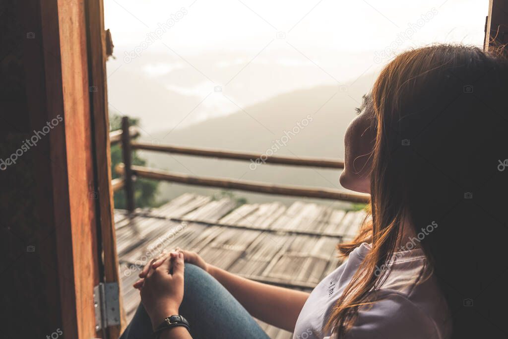 A beautiful asian woman sitting alone and looking at mountains on foggy day with blue sky background in the morning