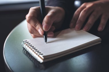 Masanın üzerine beyaz boş bir defter yazan bir kadının ellerinin yakın plan resmi. 