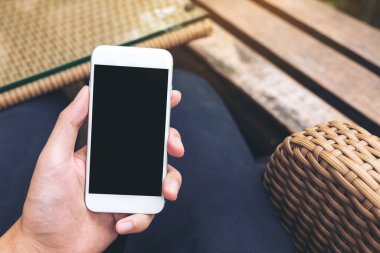 Kafede boş siyah ekranlı beyaz cep telefonu tutan bir adamın görüntüsü.