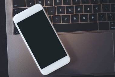 Bilgisayarın klavyesinde boş siyah masaüstü ekranı olan beyaz bir cep telefonunun en iyi görüntüsü 