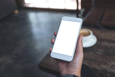 Kafedeki ahşap masada kahve fincanı ve boş masaüstü ekranı olan beyaz cep telefonlu bir kadının el resmi.
