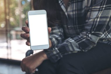 Modern kafedeki boş ekranlı beyaz cep telefonunu tutan ve gösteren bir kadının görüntüsü.