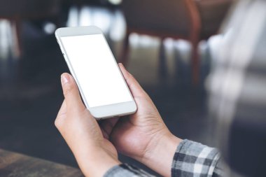 Kafedeki ahşap masada boş ekranlı beyaz cep telefonu tutan ellerin görüntüsü.