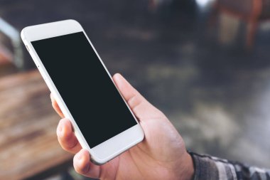 Kafedeki boş siyah ekranlı beyaz cep telefonlu el görüntüsü.