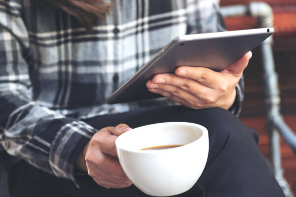 Closeup image of a woman holding and using tablet pc while drinking coffee in cafe