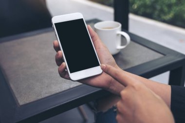 Kafedeki boş siyah masaüstü ekranlı beyaz bir cep telefonunu gösteren ve işaret eden ellerin görüntüsü