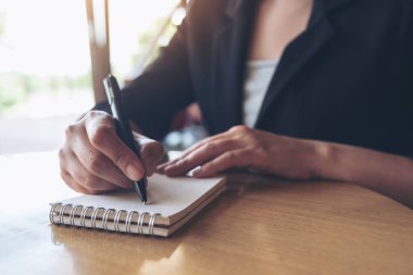 Ofisteki beyaz boş bir deftere yazı yazan bir iş kadınının yakın plan resmi.