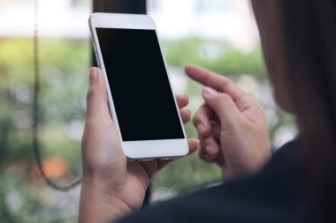Kafedeki boş siyah masaüstü ekranlı beyaz bir cep telefonunu tutan ve işaret eden kadının görüntüsü