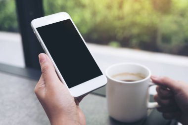 Kafede kahve içerken beyaz cep telefonu ve boş siyah masaüstü ekran görüntüsü.