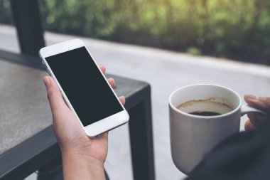 Kafede kahve içerken beyaz cep telefonu ve boş siyah masaüstü ekran görüntüsü.