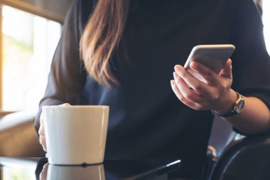 Kafede kahve içerken elinde telefon tutan ve kullanan bir kadının yakın plan görüntüsü.