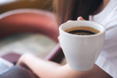 Sabahları içmeden önce elinde kahve fincanı tutan bir kadın resmi.