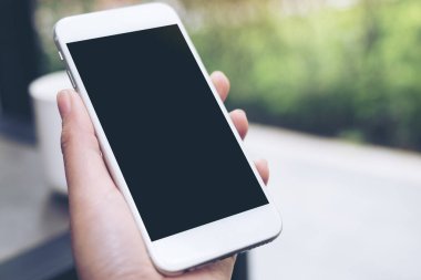 Kahve masasında kahve fincanı olan, boş siyah masaüstü ekranlı, beyaz cep telefonlu el resmi.
