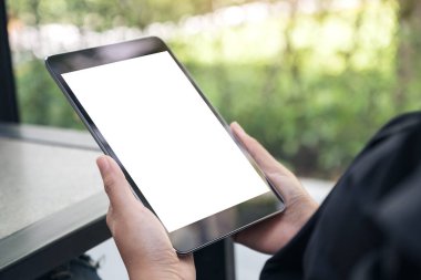 Masada boş beyaz masaüstü ekranı olan siyah tableti tutan ellerin görüntüsü