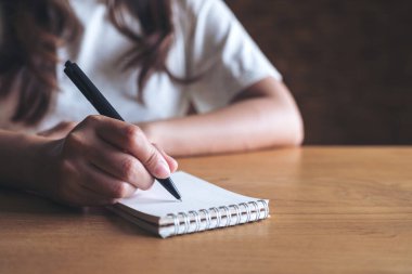 Masaya beyaz boş bir defter yazan bir kadının yakın plan resmi. 
