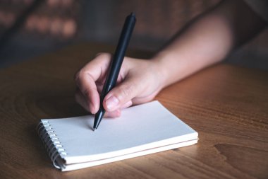 Tahta masaya beyaz boş bir defter yazan bir elin yakın plan resmi. 