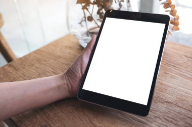 Boş beyaz masaüstü ekranlı siyah tableti tutan el resmi ahşap masa üzerinde