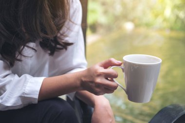Sabahları içmeden önce elinde kahve fincanı tutan bir kadın resmi.