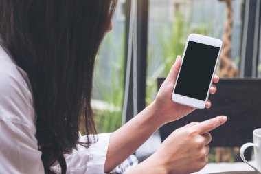 Kafedeki boş siyah ekranlı beyaz cep telefonunu tutan ve gösteren bir kadının görüntüsü.