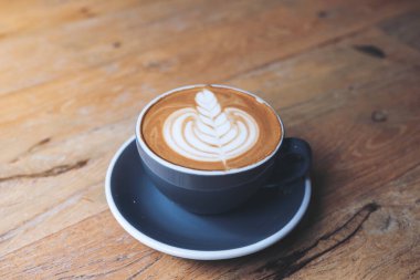 Kafedeki eski ahşap masada latte sanatıyla birlikte mavi bir fincan sıcak latte kahvenin yakın plan görüntüsü.