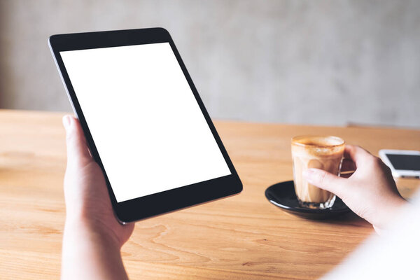 Изображение женщины, держащей черный планшет с чистым белым экраном рабочего стола во время питья кофе в кафе
