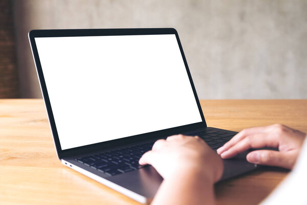 Mockup image of a woman using and typing on laptop with blank white desktop screen on wooden table 