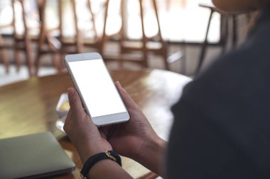 Kafedeki boş masaüstü ekranlı beyaz cep telefonu tutan bir kadının ellerinin görüntüsü.