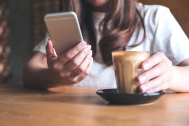Bir kadının elinde tuttuğu, kahve içerken akıllı bir telefona dokunduğu yakın plan görüntüsü.