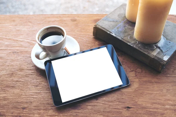 Top view mock up image of black tablet with white blank desktop screen and coffee cup , book , candles on vintage wooden table in cafe