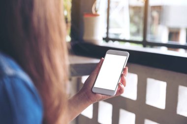 Kafede boş masaüstü ekranı olan beyaz cep telefonu tutan bir kadının görüntüsü
