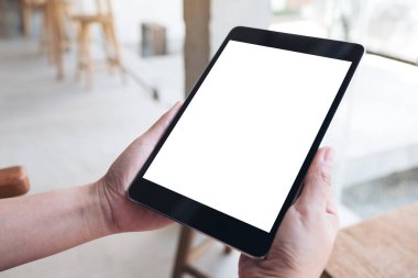 Ahşap masanın üzerinde boş beyaz masaüstü ekranı olan siyah tableti tutan ellerin görüntüsü