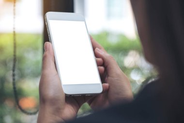 Kafede boş masaüstü ekranı olan beyaz bir cep telefonu tutan ve kullanan kadının görüntüsü