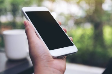 Kahve masasında kahve fincanı olan, boş siyah masaüstü ekranlı, beyaz cep telefonlu el resmi.