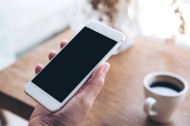 Kafedeki boş siyah masaüstü ekranlı beyaz cep telefonlu el görüntüsü